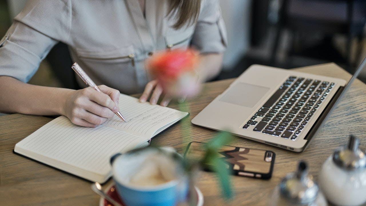 Quelle: Pexels (https://www.pexels.com/de-de/foto/person-die-auf-einem-notizbuch-neben-macbook-schreibt-1766604/)